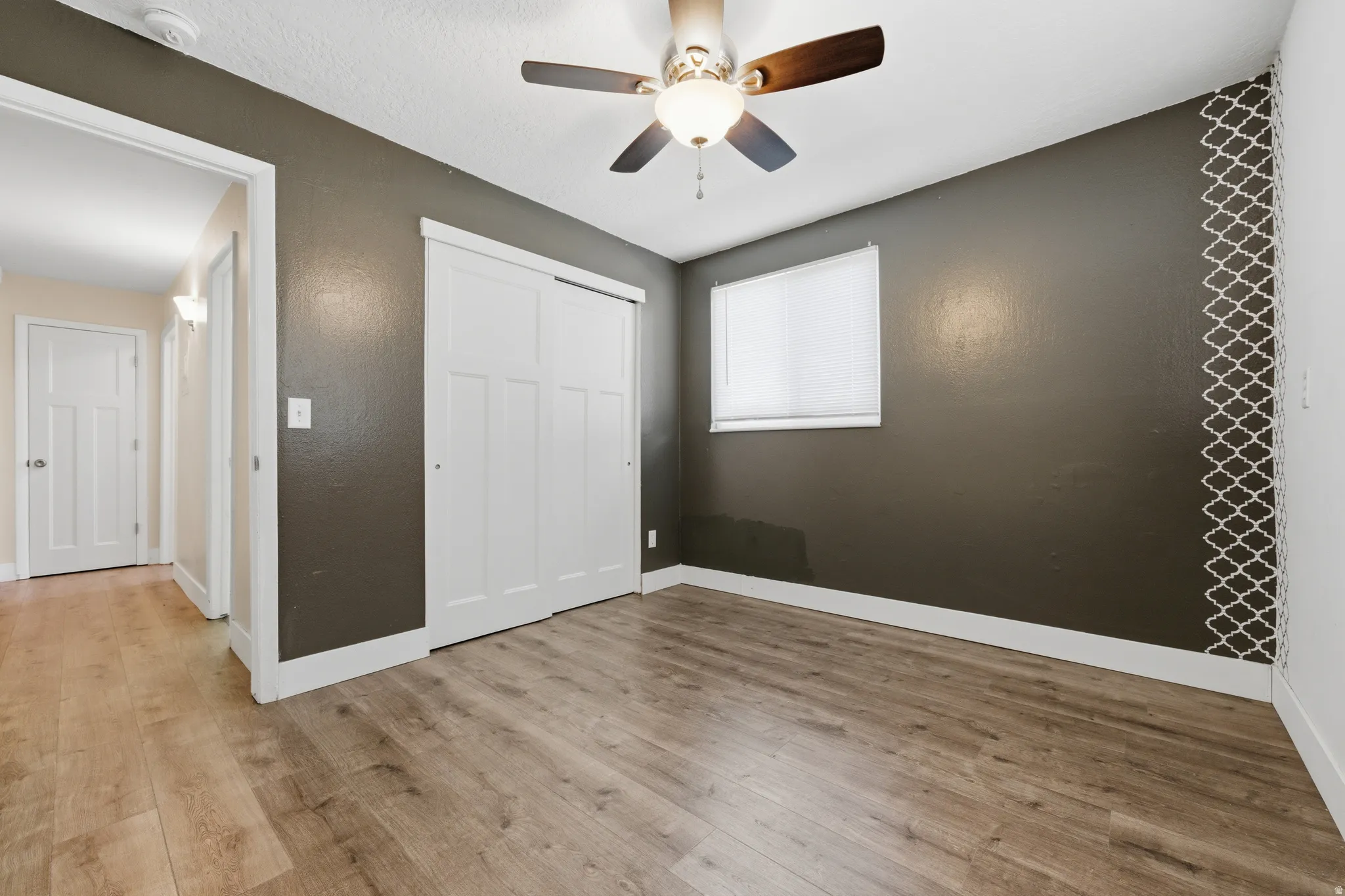 Interior room featuring wood-finish flooring, a ceiling fan with light fixture, and a window with blinds