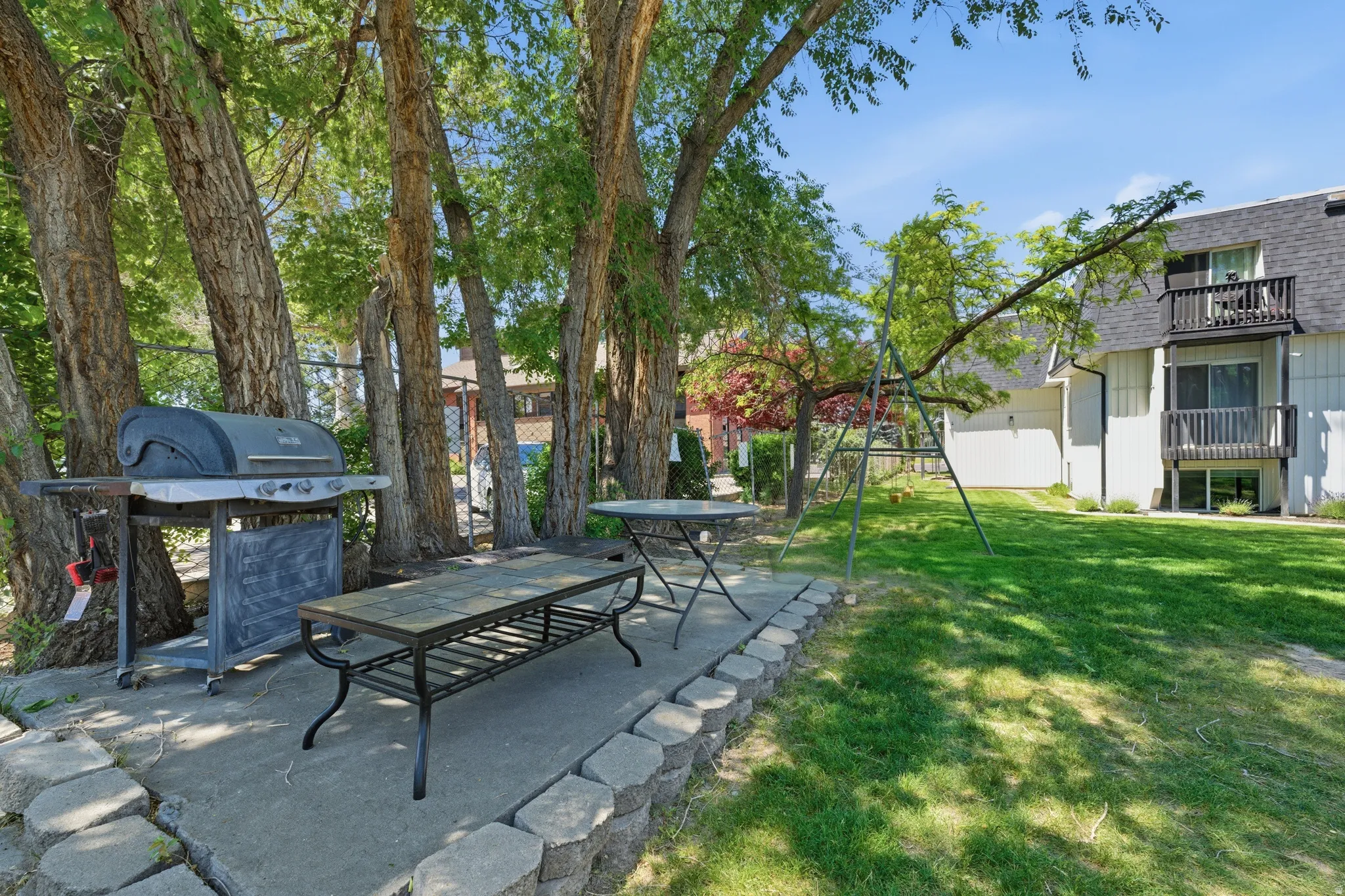 Outdoor patio area featuring a concrete pad, a low retaining wall with stone blocks, and mature trees providing natural shading