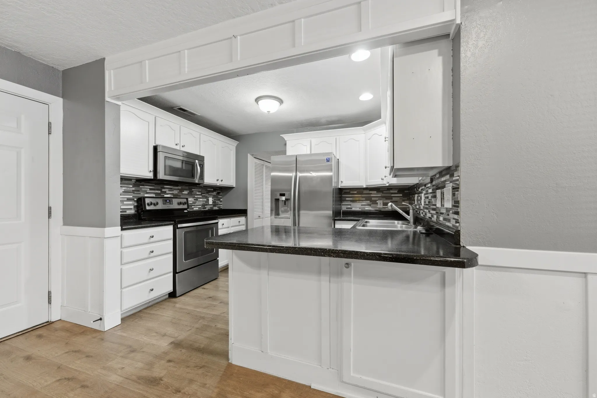 Kitchen featuring white cabinetry, dark countertops, a mosaic tile backsplash, and stainless steel appliances