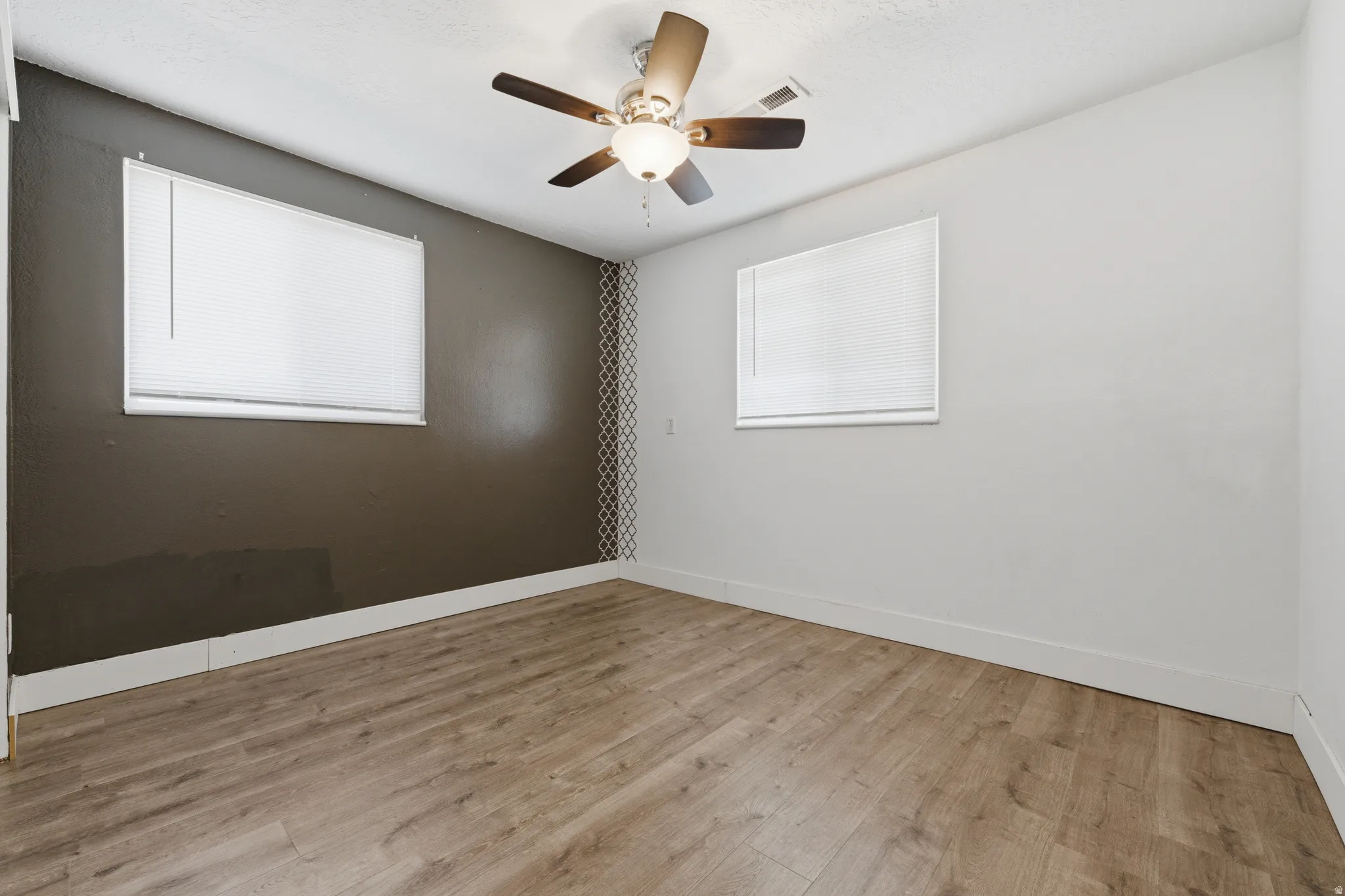 Spacious room with wood-finish flooring, a contemporary ceiling fan, and distinct accent walls featuring a geometric pattern and a contrasting solid tone