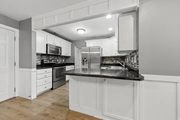 Kitchen featuring white cabinetry, dark countertops, a mosaic tile backsplash, and stainless steel appliances