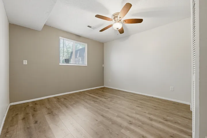 Spacious room featuring wood-finish flooring, a ceiling fan with integrated lighting, and a window for natural illumination