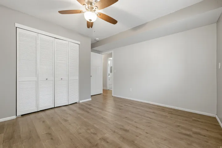 Spacious room featuring wood-finish flooring, light gray walls, and a ceiling fan with integrated lighting