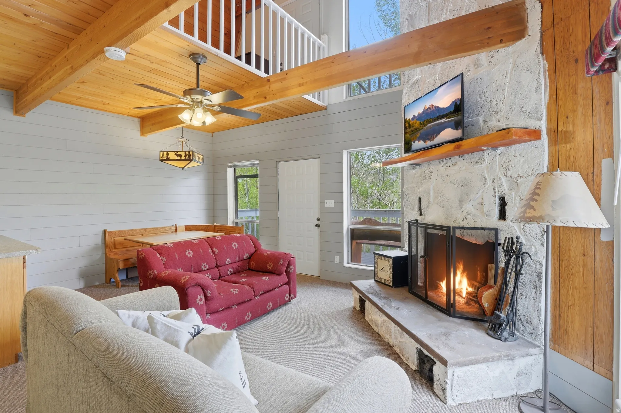 Living area featuring a stone fireplace with a raised hearth, wood-finish flooring, exposed wood ceiling beams, and a mezzanine with white railings