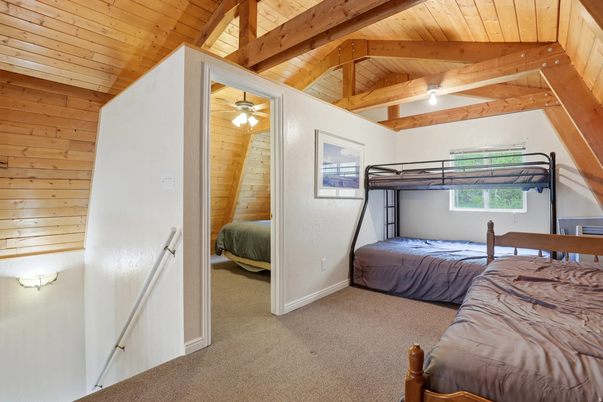 Carpeted loft area featuring exposed wood beams, a window, and a doorway opening to an additional room