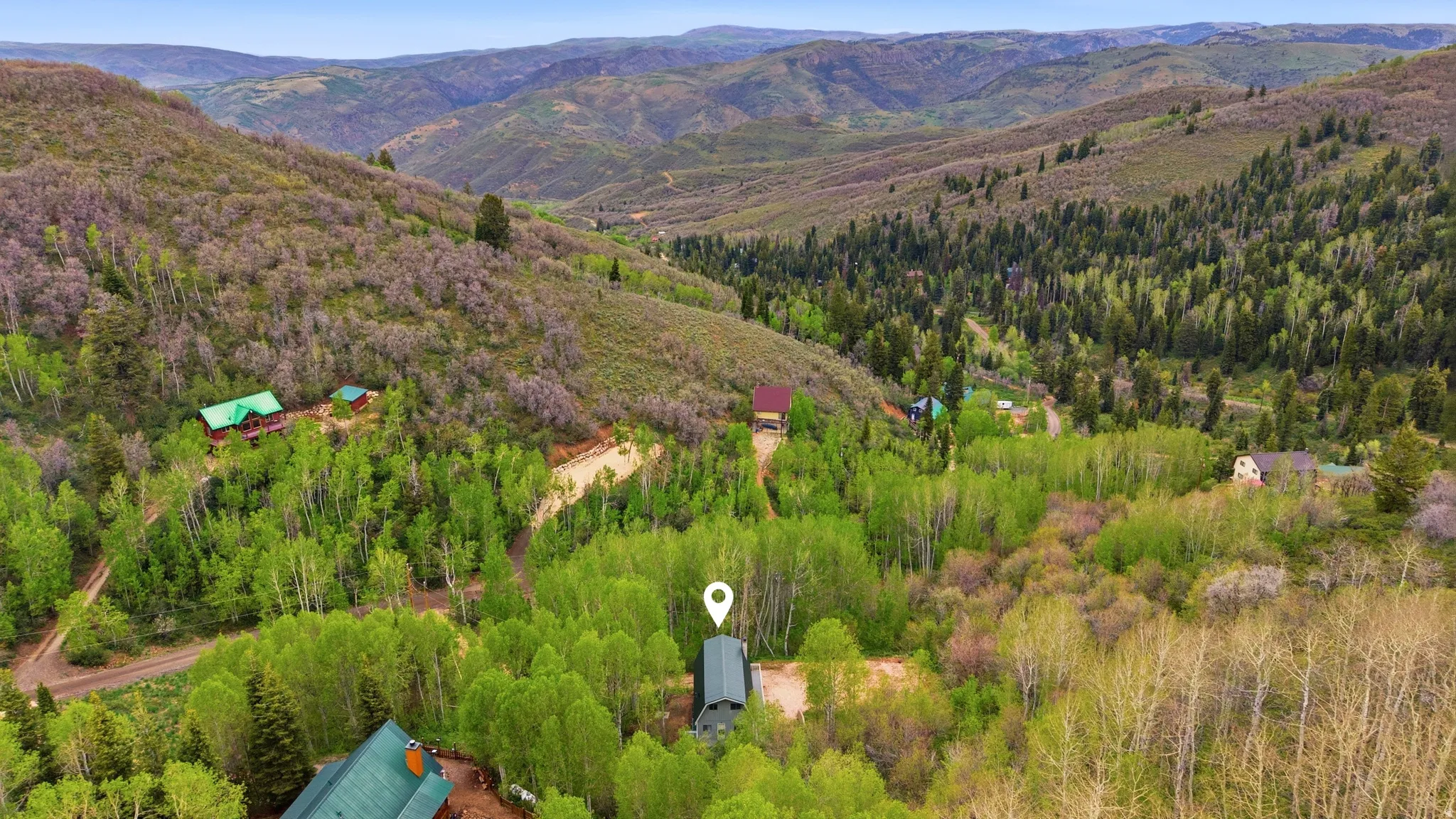Mountainous landscape featuring a verdant valley, multiple residential structures, dense tree coverage, and winding terrain