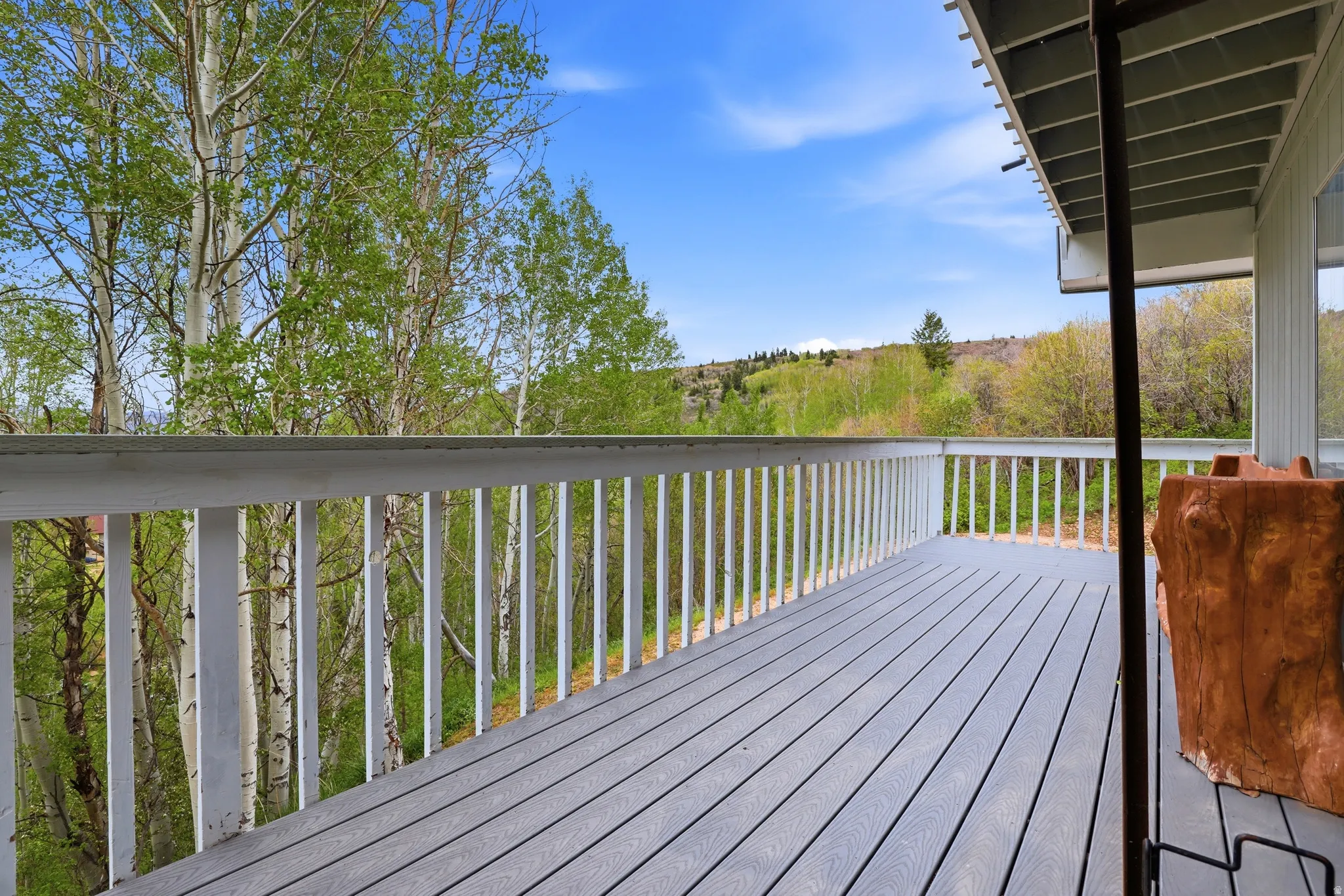 Spacious outdoor deck featuring gray composite decking and white railing, overlooking a lush green landscape with mature trees