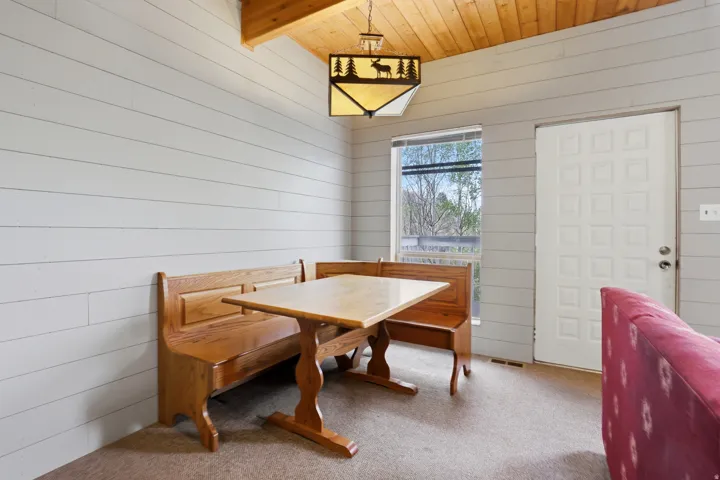 Vaulted wood-paneled ceiling with a decorative pendant light fixture, shiplap-style walls, carpeted flooring, and a window providing natural illumination