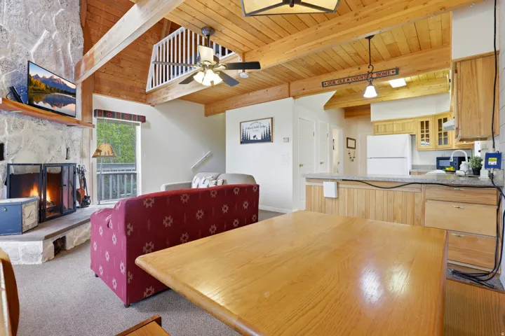 Vaulted wood-paneled ceilings with exposed beams, a stone-faced fireplace, a kitchen island with beadboard paneling, and wood-finish flooring