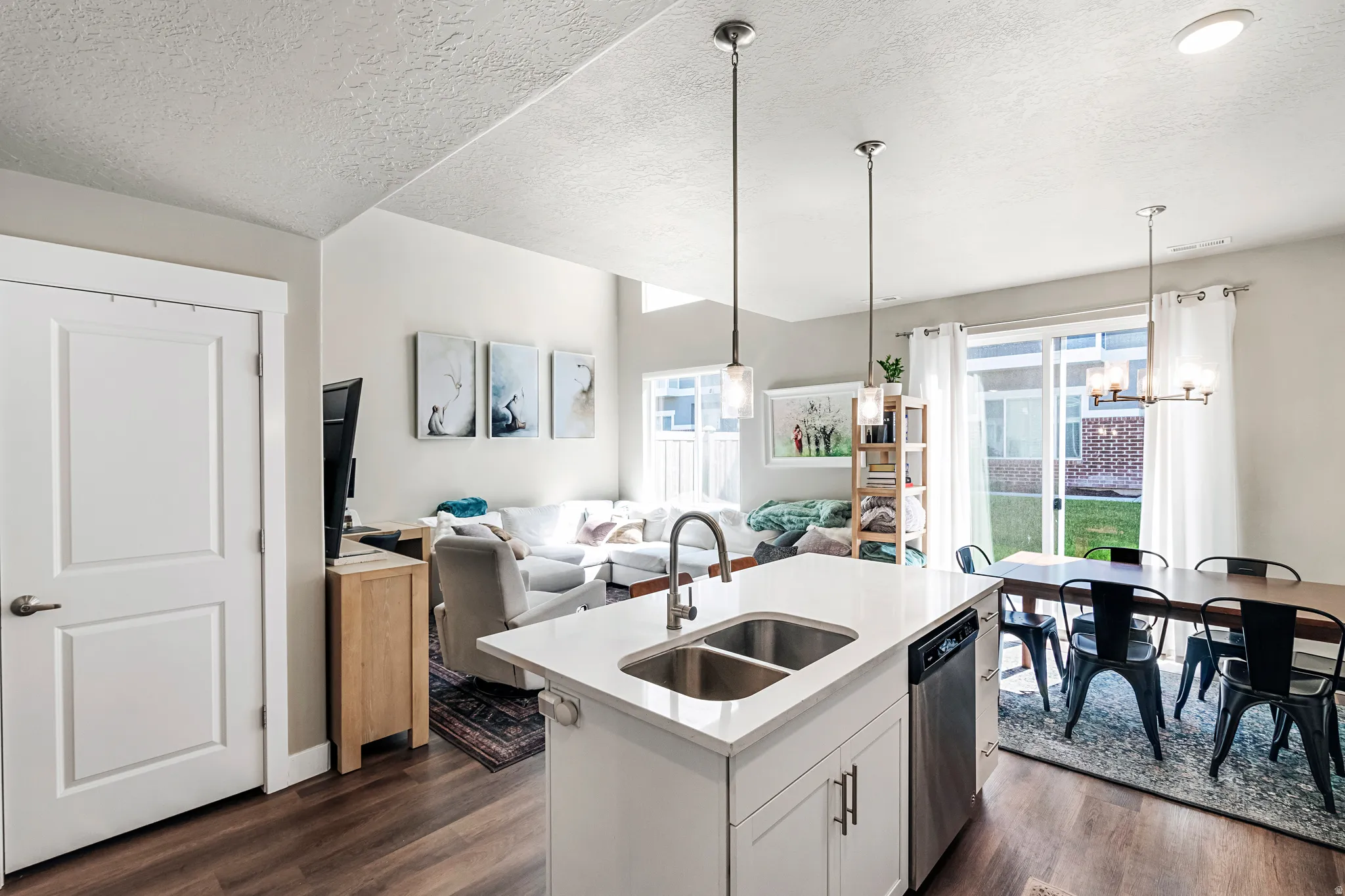 Open-concept interior featuring wood-finish flooring, a kitchen island with dual pendant lighting, stainless steel appliances, a sliding glass door, and recessed lighting