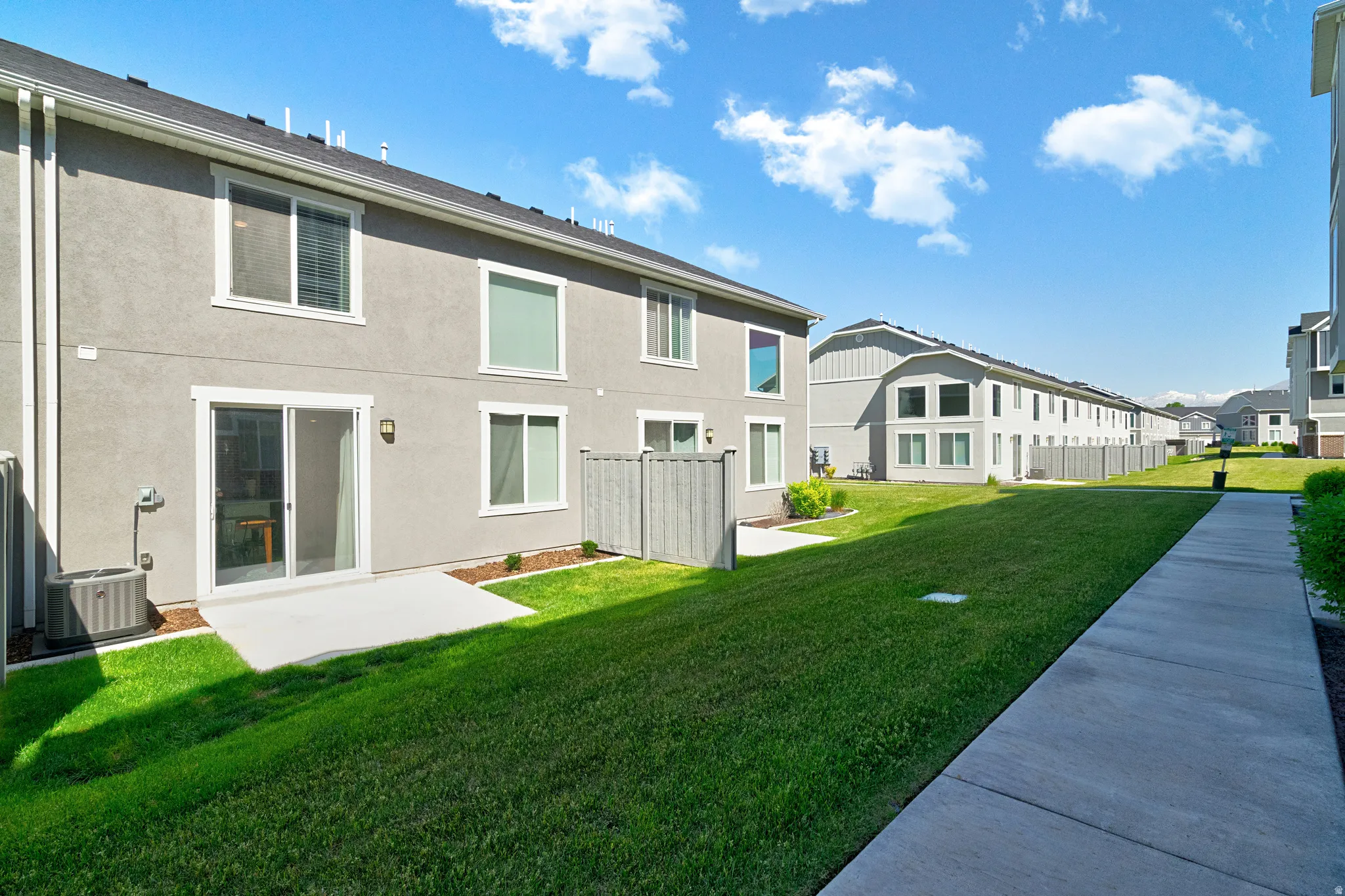 Manicured green space featuring a concrete patio, sliding glass door, and a privacy fence