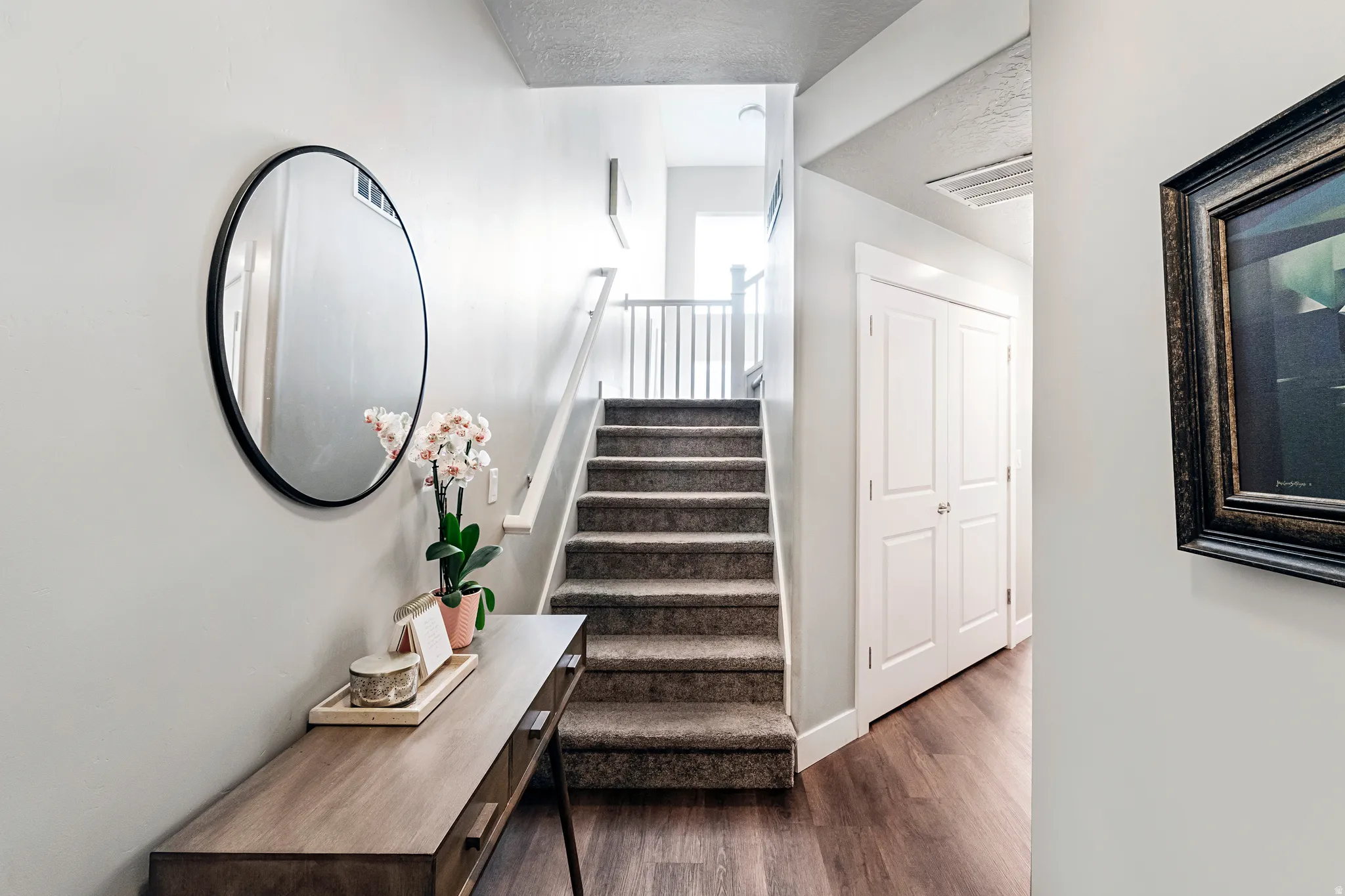 Entryway featuring wood-finish flooring, a carpeted staircase with white railings, and a built-in double-door closet