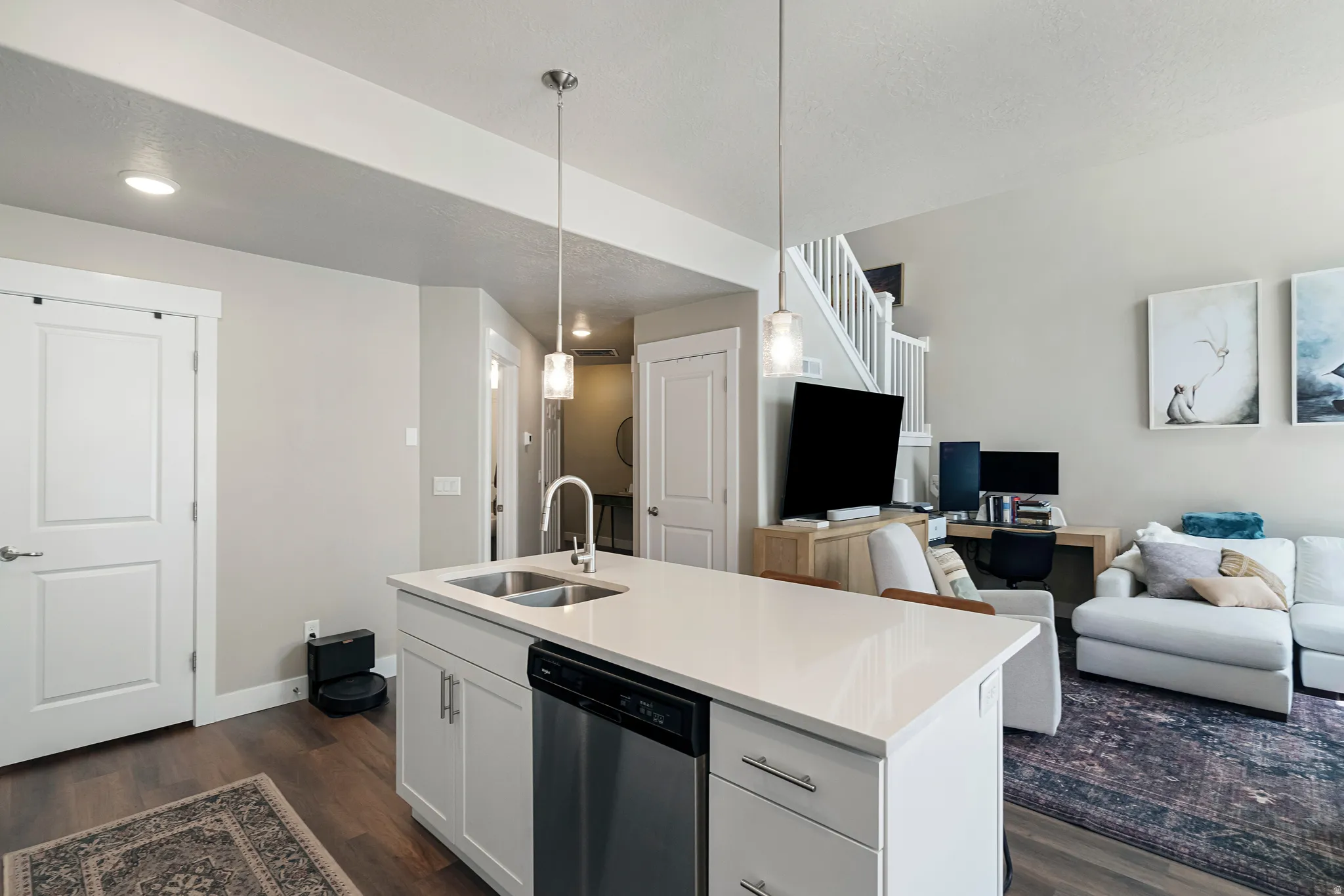 Kitchen island featuring a double-basin sink, stainless steel dishwasher, white cabinetry, and a light-toned countertop