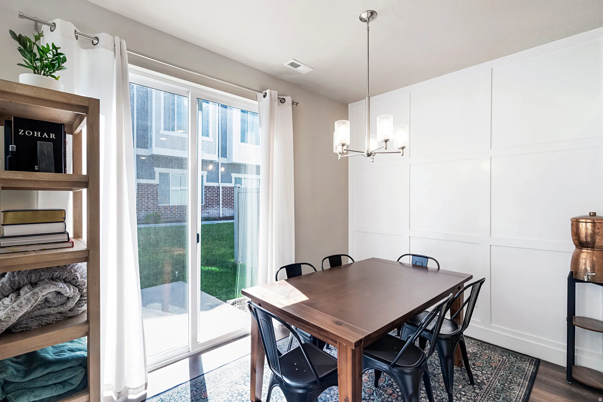 Dining area featuring a contemporary chandelier, board and batten accent wall, wood-finish flooring, and a sliding glass door providing access to a private patio and green space