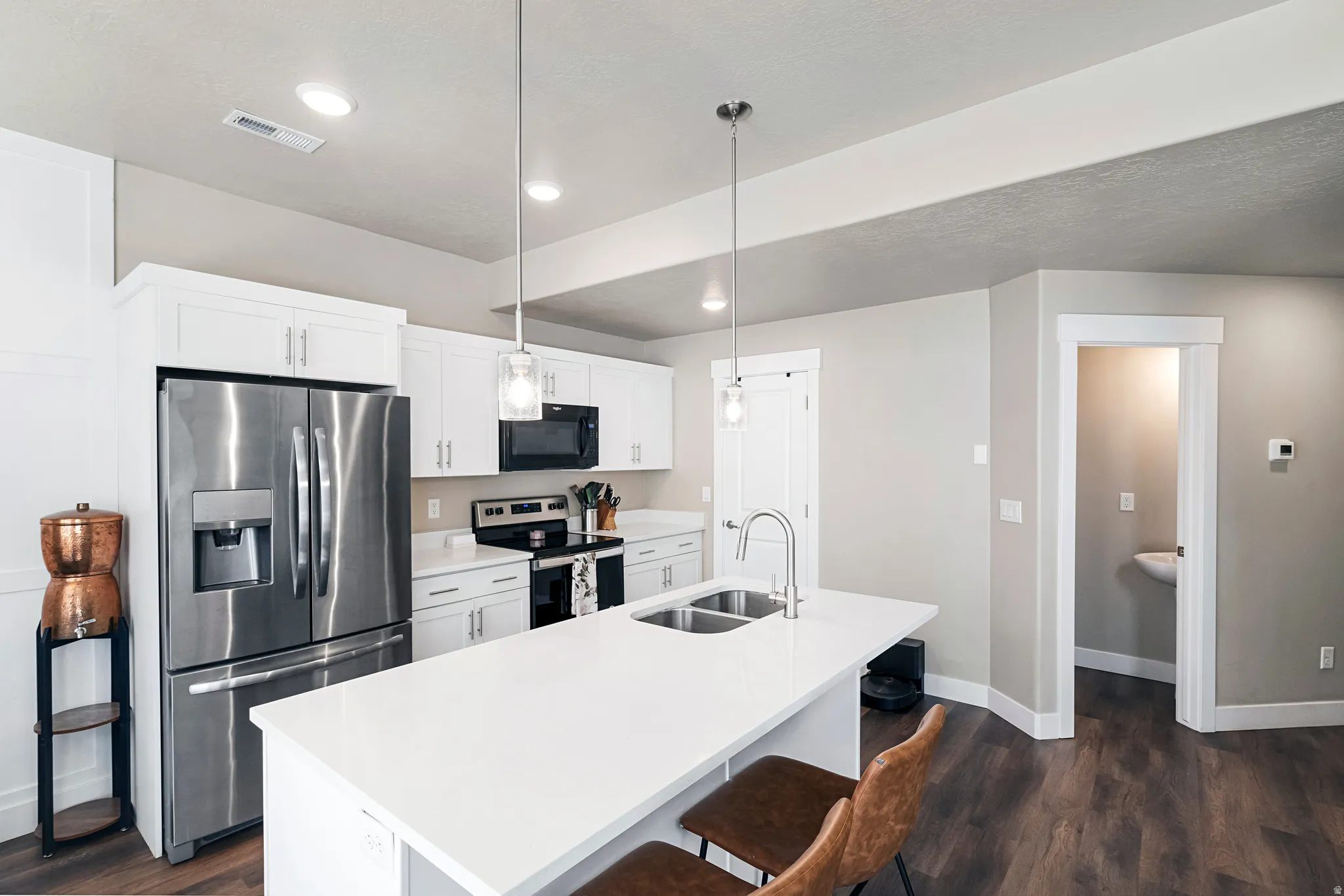 Kitchen featuring white cabinetry, stainless steel appliances, a center island with a double basin sink, and pendant lighting