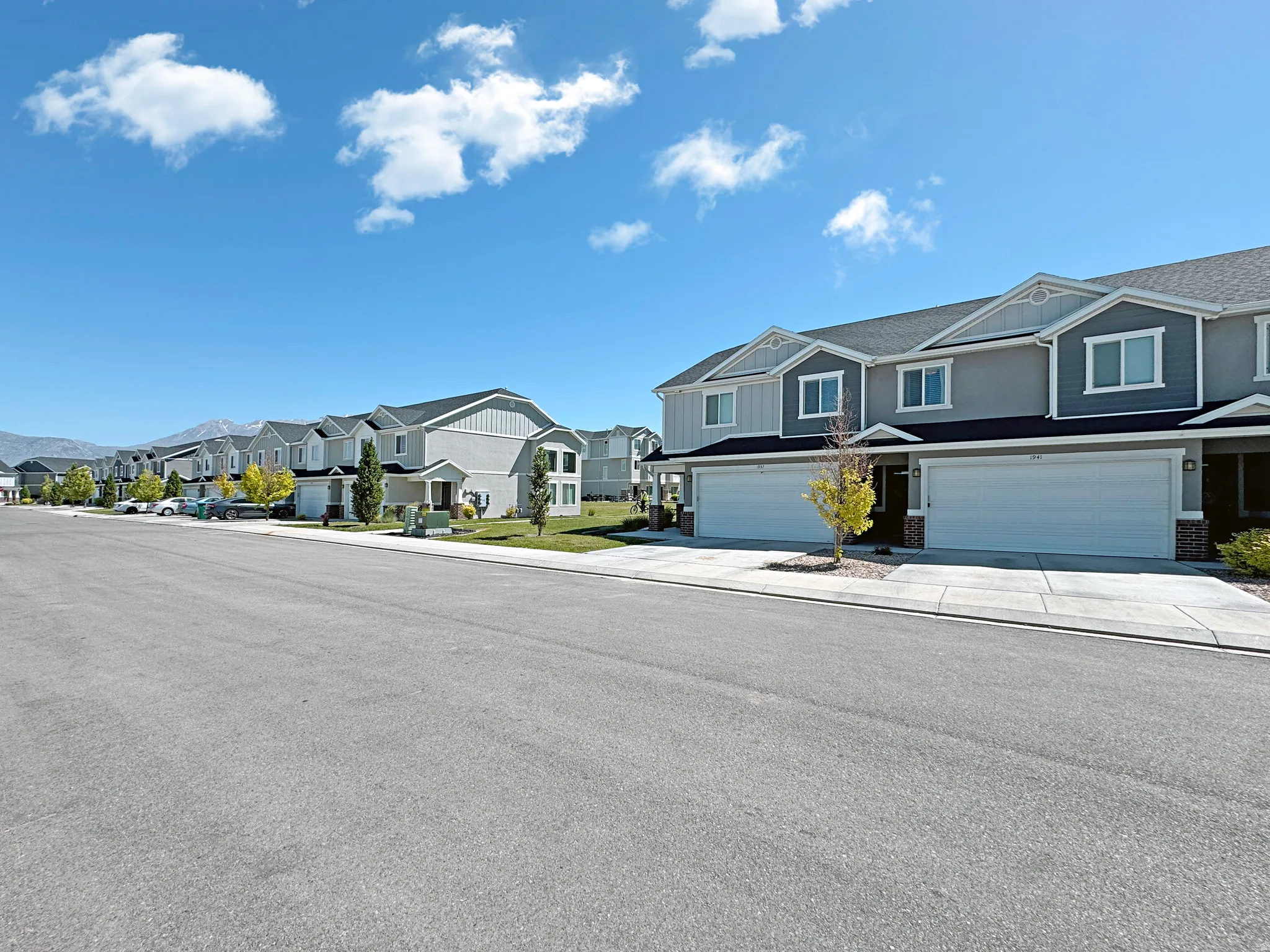 Modern townhome exterior featuring a two-car garage, gray siding, white trim, and a concrete driveway