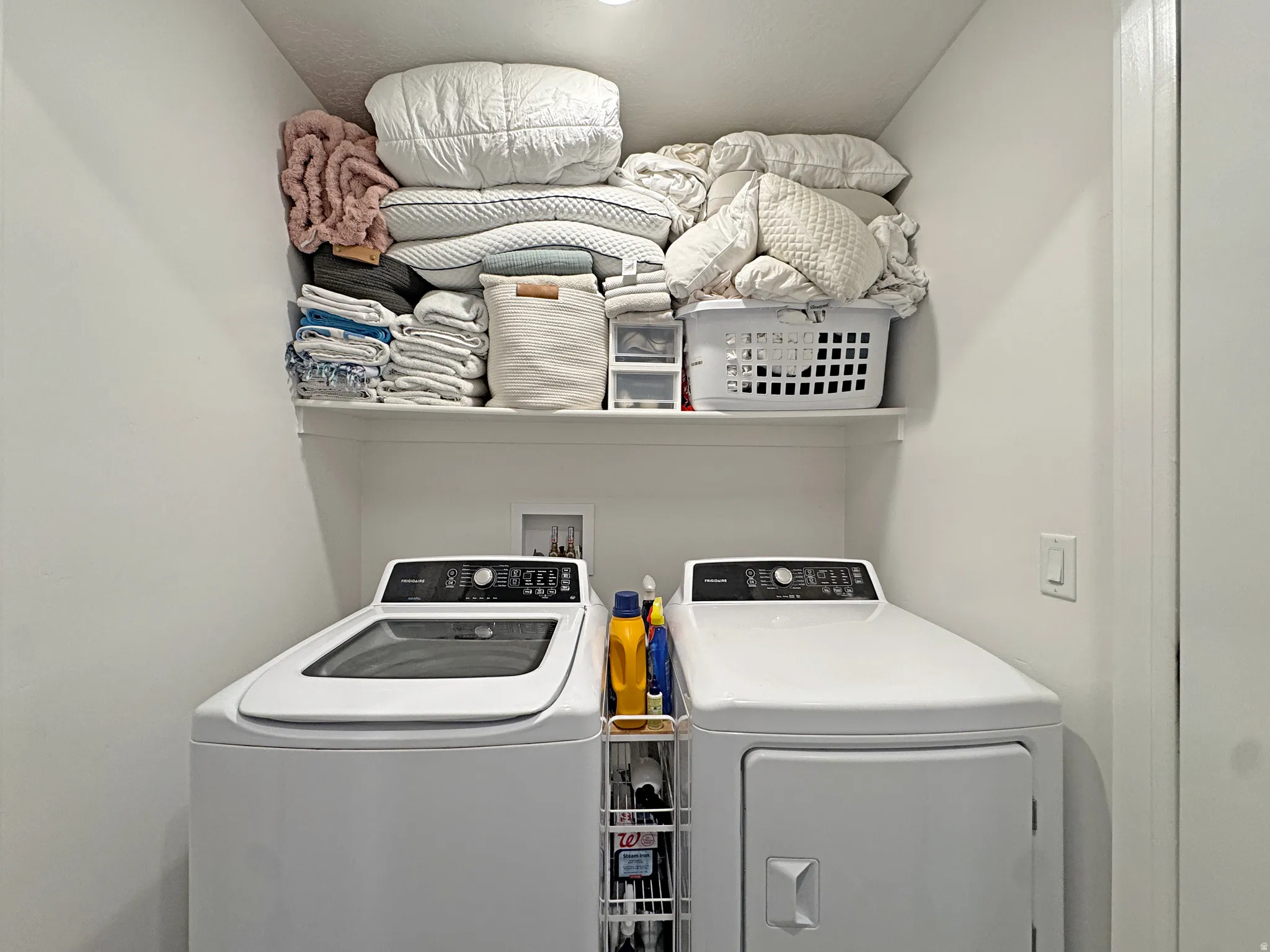 Dedicated laundry area featuring a top-load washing machine, front-load dryer, and overhead built-in shelving