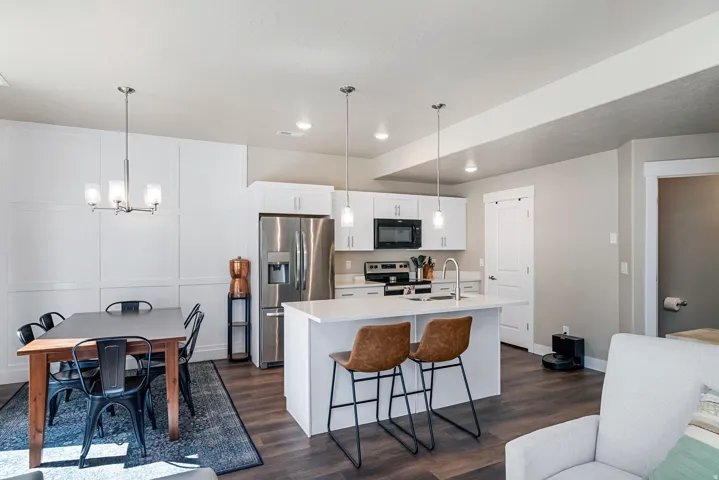 Open-concept kitchen and dining area featuring wood-finish flooring, white cabinetry, a kitchen island with seating, stainless steel appliances, and pendant lighting