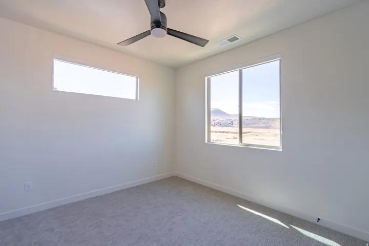 Light-filled room featuring a broad window, a horizontal transom window, a ceiling fan, and light gray carpeting