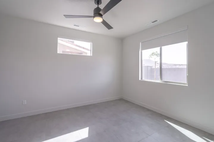 Spacious room featuring a modern ceiling fan, two windows, and light gray tile flooring