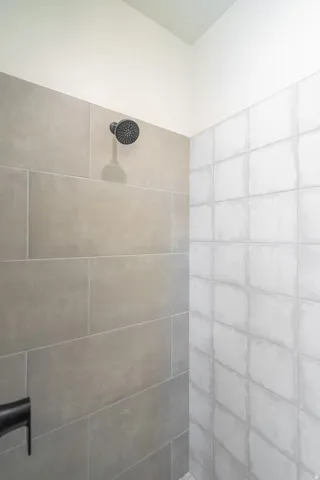 Shower enclosure featuring large format grey wall tiles, textured white square tiles, and a matte black shower head