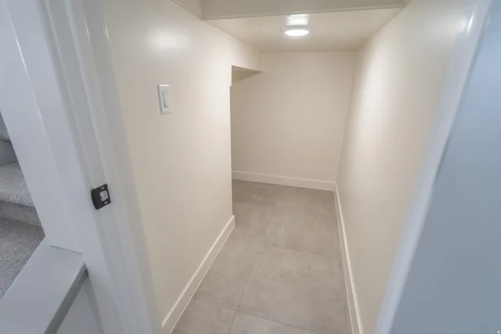 Lower-level hallway featuring light gray tile flooring, crisp white baseboards, and neutral wall paint