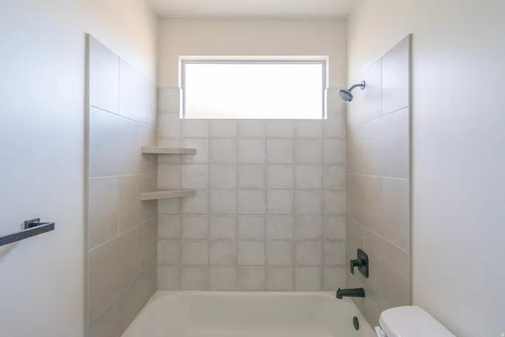 Bathroom featuring a white bathtub, light-toned wall tiling, and a transom window