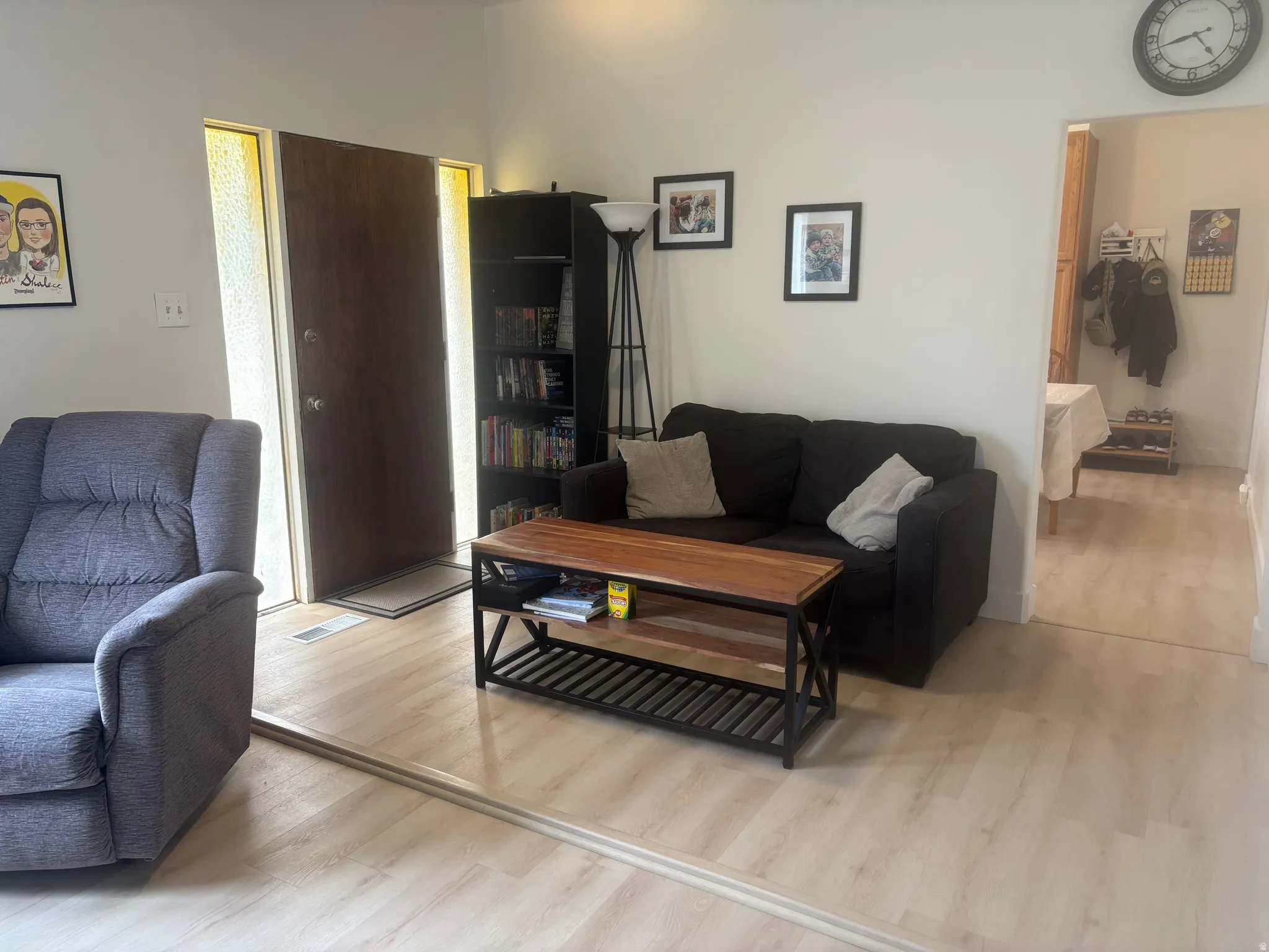 Light-toned wood-finish flooring extends throughout the living area, featuring a front entry door with vertical sidelight windows