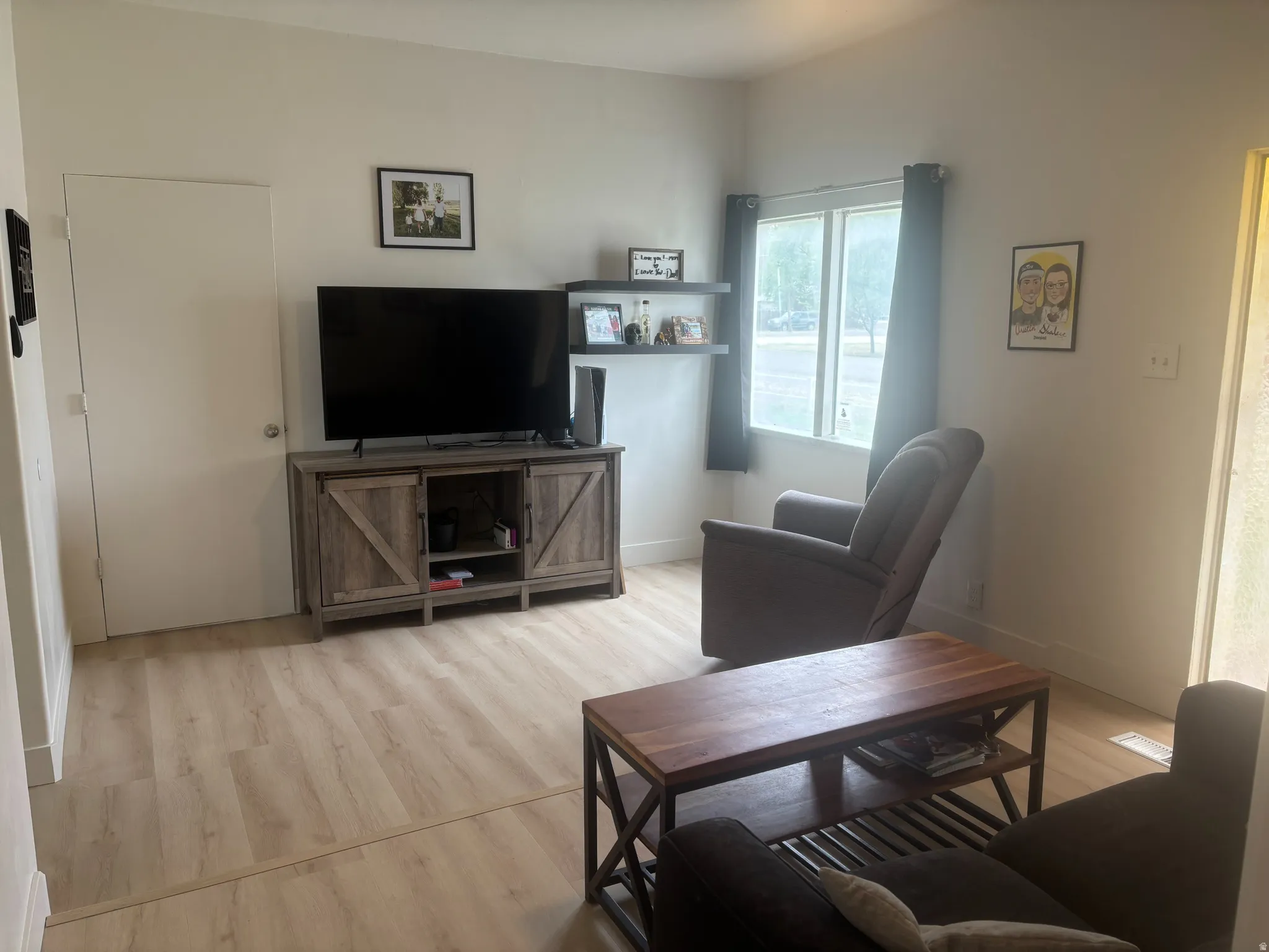 Laminate wood-finish flooring throughout, featuring a window with dark curtains, and a barn door-style media console