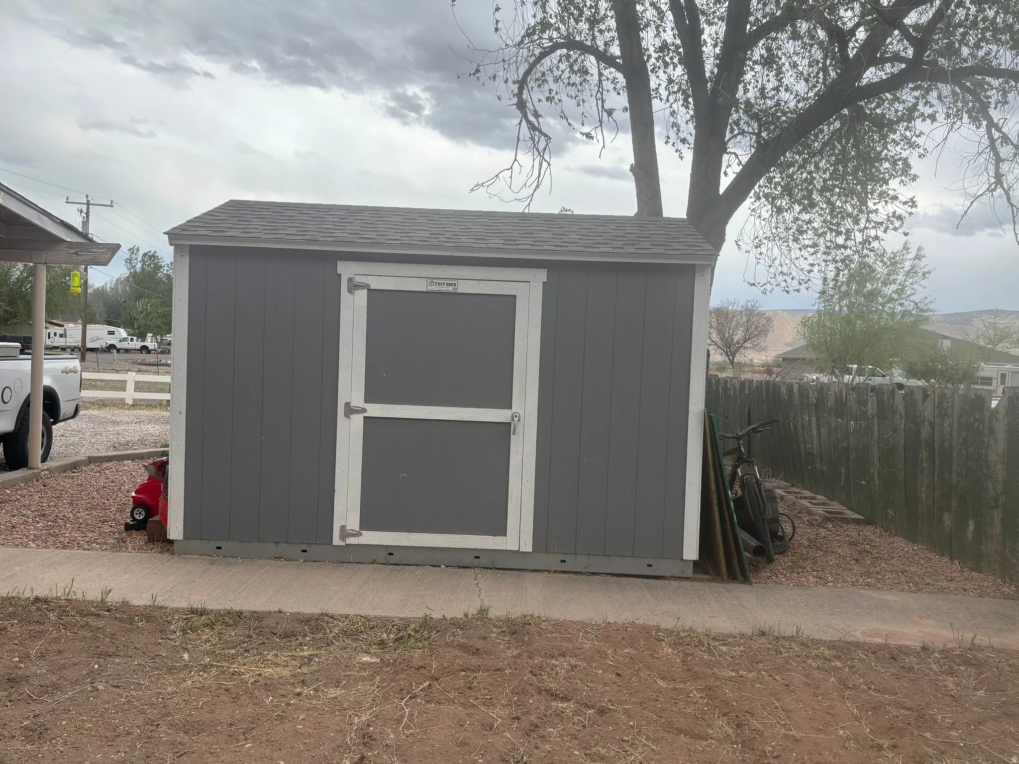Exterior storage shed featuring vertical gray siding, white trim, and a shingled roof
