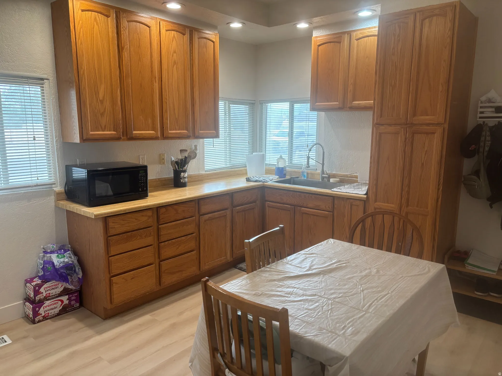 Kitchen featuring extensive oak cabinetry, a corner sink with a window, light wood-finish flooring, recessed lighting, and ample counter space