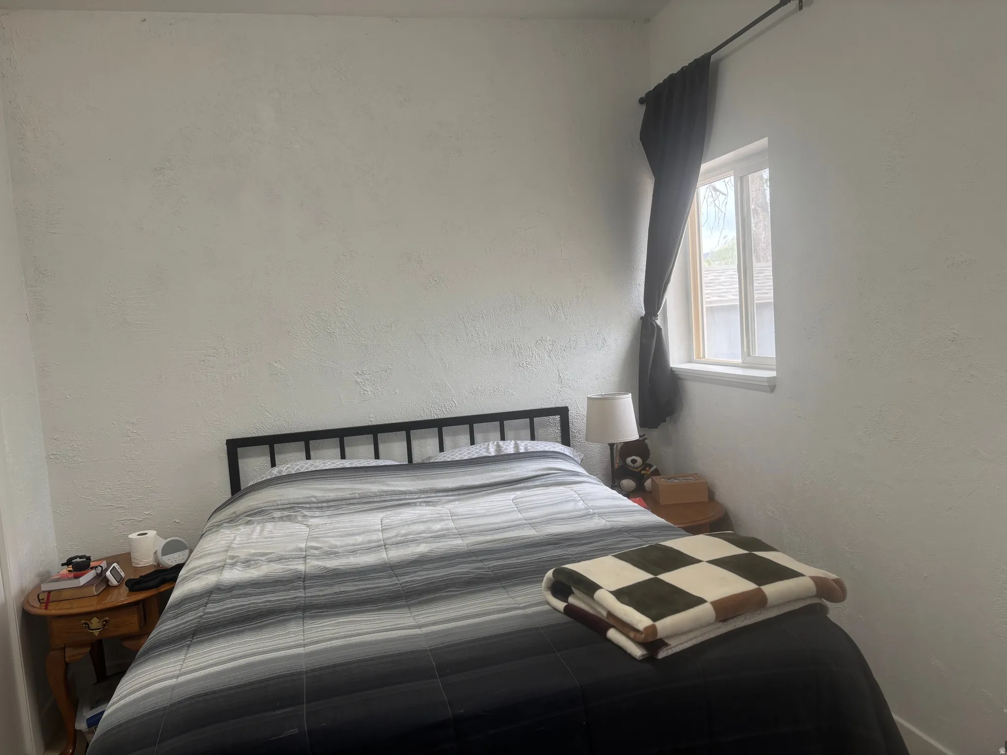 Bedroom with textured white walls, 2 windows, and dark window treatment