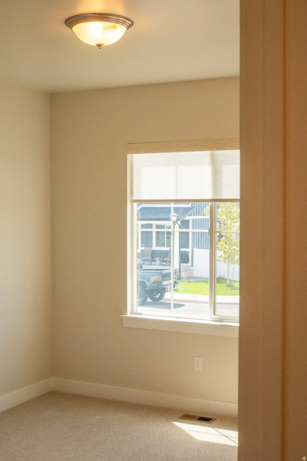 Room featuring a single window with a roller shade, neutral wall paint, and beige carpeting