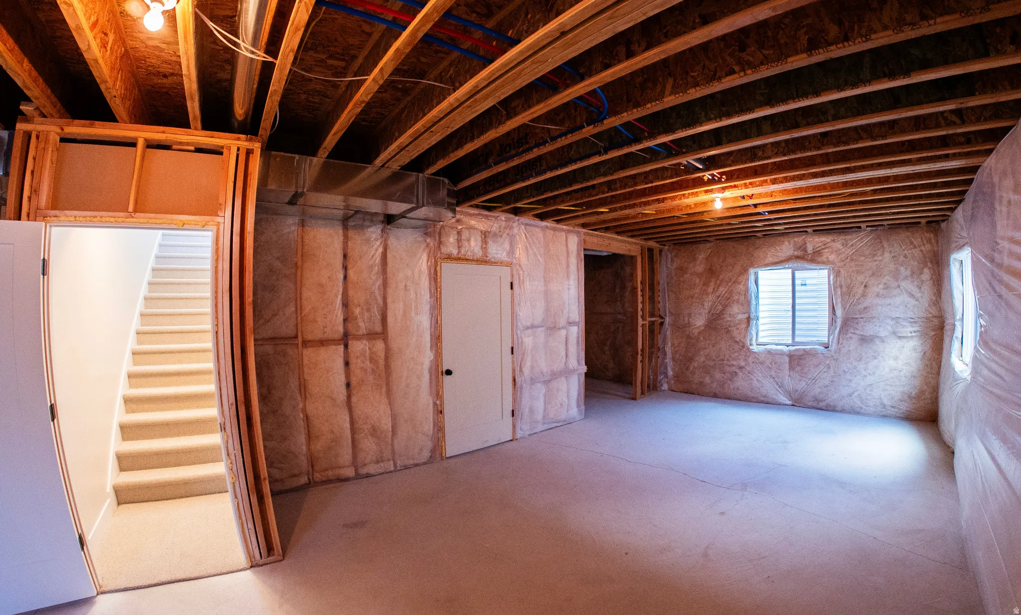 Unfinished basement featuring exposed wood joists, concrete flooring, insulated walls, and a visible egress window