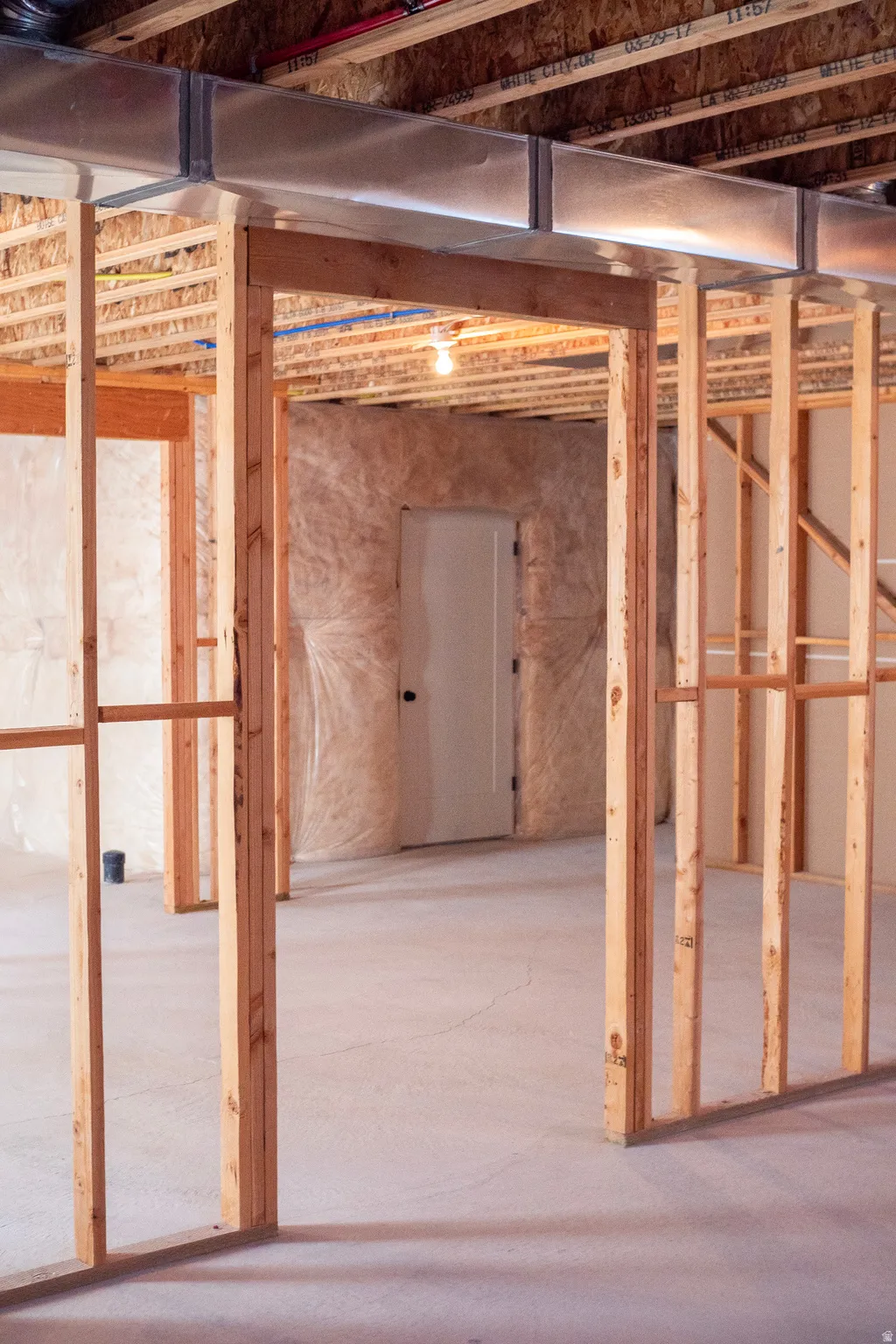 Unfinished basement featuring exposed wood framing, concrete flooring, and an existing doorway