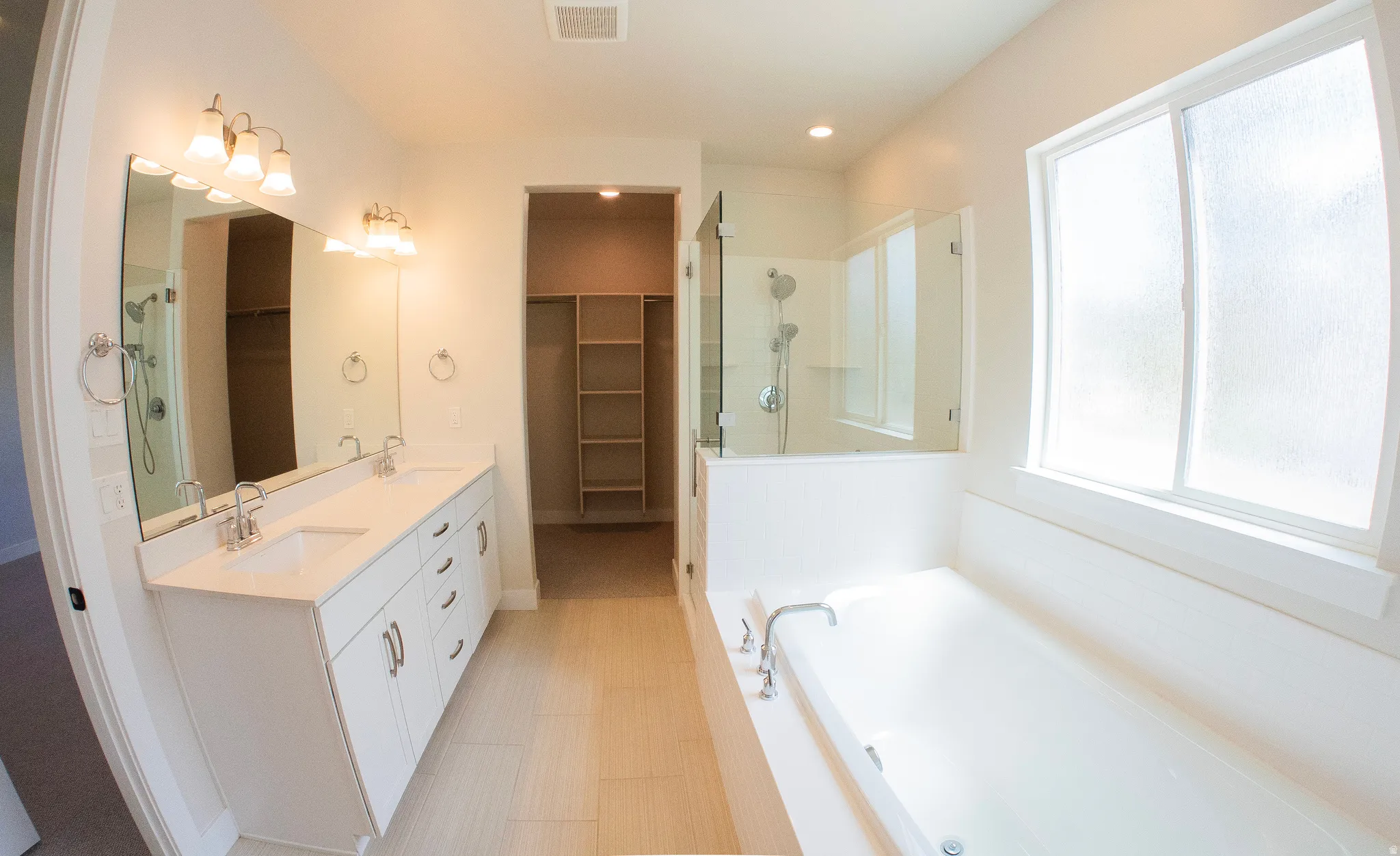 Spacious bathroom featuring a dual vanity with white cabinetry, a built-in soaking tub, and a glass-enclosed shower