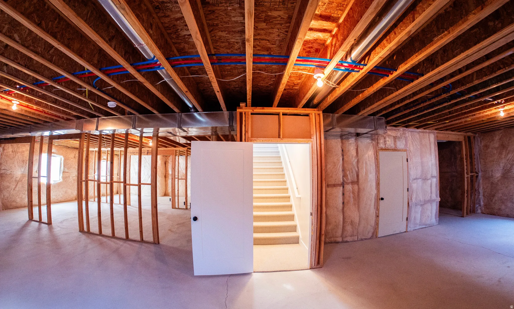 Unfinished lower level featuring exposed ceiling joists, framed interior walls, visible plumbing lines, ductwork, and an interior staircase
