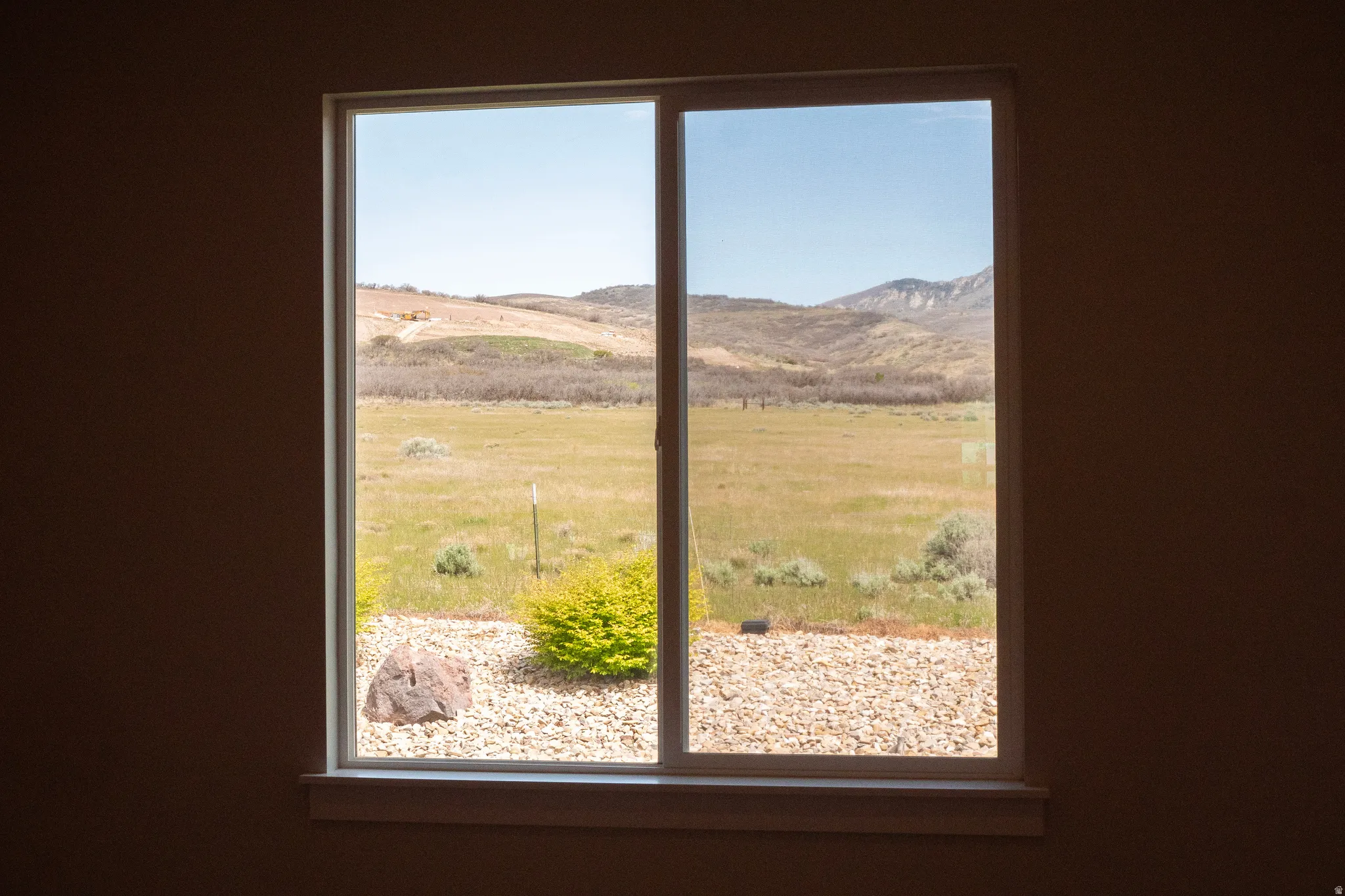 Double-pane window featuring a distant mountain landscape, a green field, and a rock garden with a prominent boulder and shrubbery