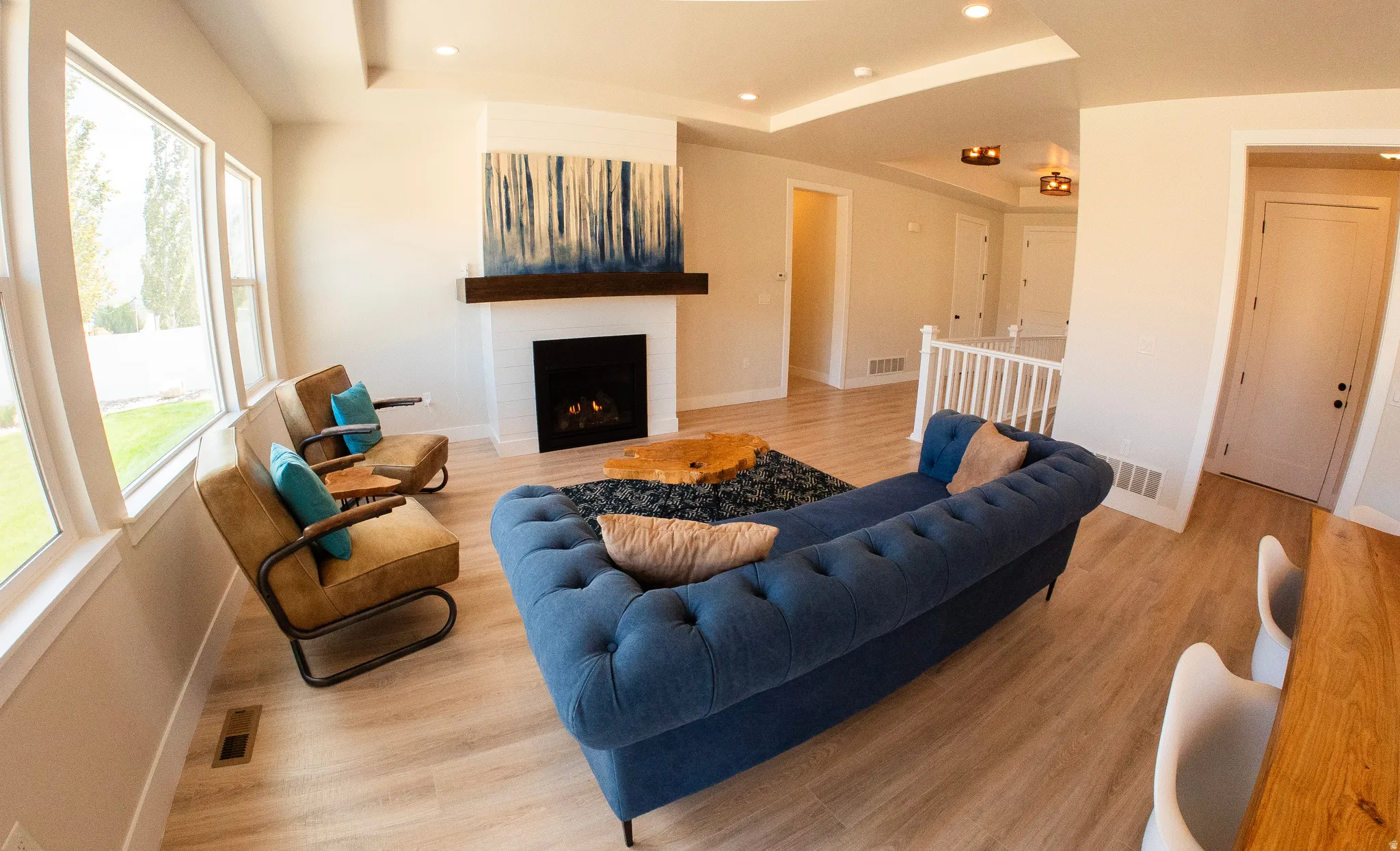 Spacious living area featuring light wood-finish flooring, a contemporary fireplace with a white tile surround and wood mantle, and large windows