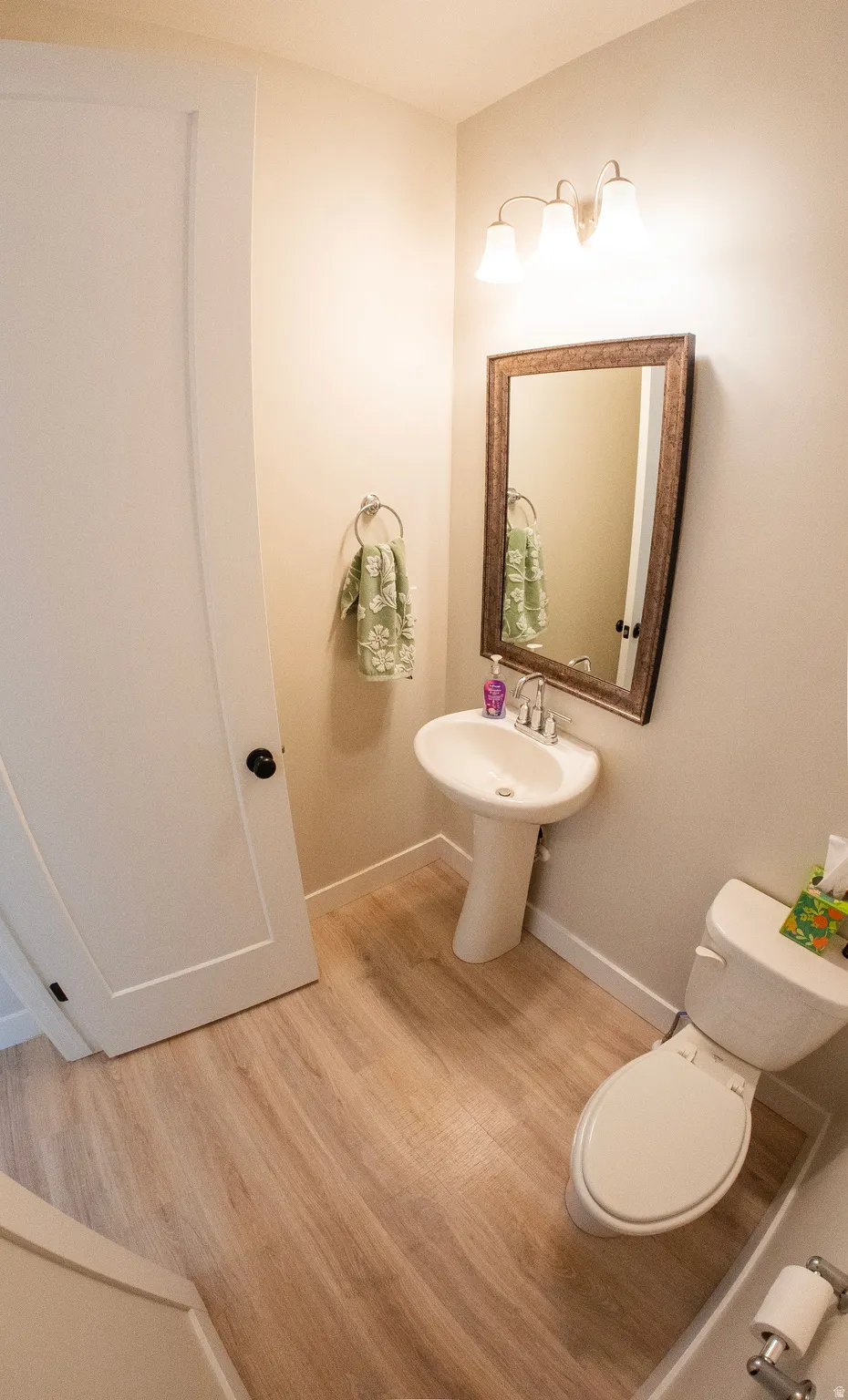 Pedestal sink with chrome faucet, framed mirror, and three-bulb vanity lighting