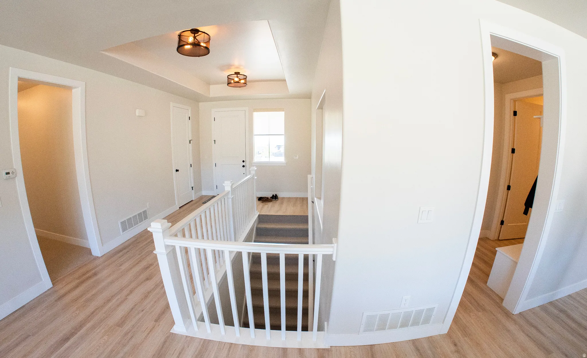 Hallway landing featuring wood-finish flooring, white spindle railing, tray ceiling with two semi-flush mount light fixtures, and white paneled doors