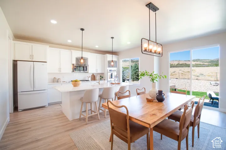 Open-concept kitchen and dining area featuring white cabinetry, a kitchen island with seating, pendant lighting, and wood-finish flooring