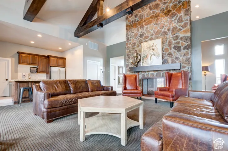 Vaulted ceilings with exposed wood beams, stone fireplace, and a built-in wet bar with wood cabinetry and stainless steel appliances