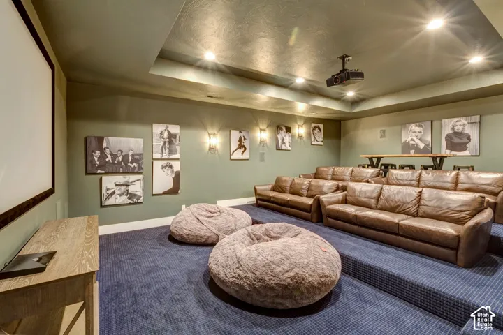 Dedicated media room featuring tiered seating, recessed ceiling lighting, a mounted projector, and a large projection screen
