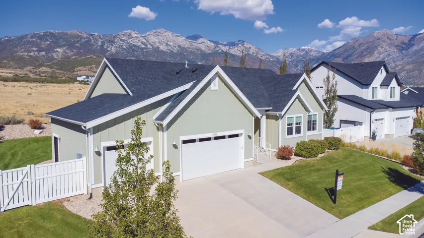 Light green siding exterior with white trim, a dark shingle roof, attached garages, and a paved driveway, set against a mountain backdrop