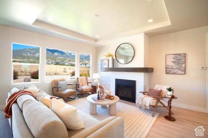 Bright living area with recessed lighting, a tray ceiling, wood-finish flooring, and a fireplace with a wood mantle and tile surround