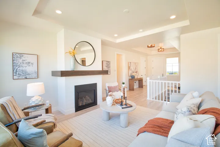 Recessed lighting, tray ceiling, fireplace with wood-finish mantel, and light wood-finish flooring