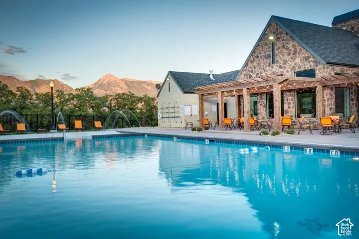 Expansive outdoor pool area featuring a stone-clad building with a covered patio, string lights, and mountain scenery