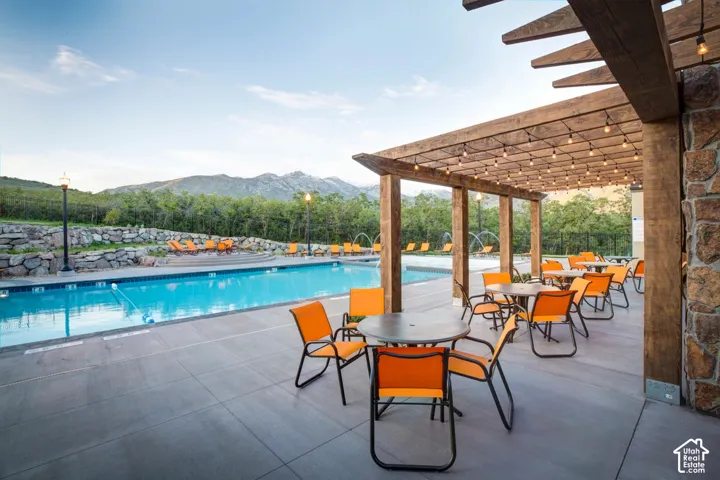 Expansive outdoor swimming pool with a surrounding stone wall, large wood pergola, string lighting, and mountain backdrop