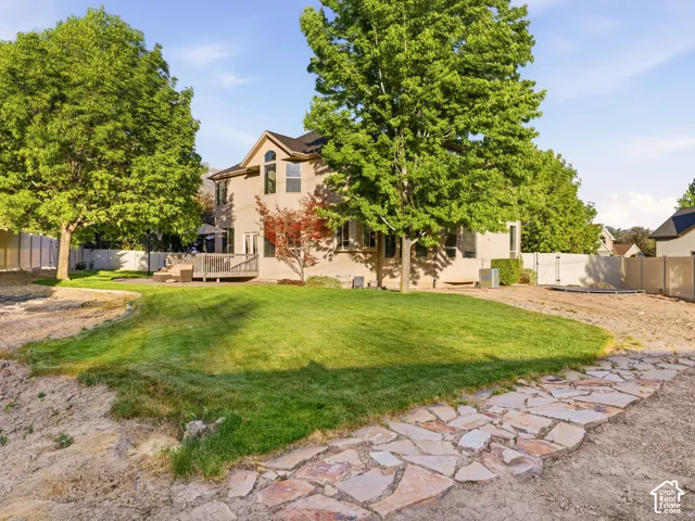 Rear exterior featuring a spacious lawn, mature trees, a multi-level wood deck, and a stone pathway